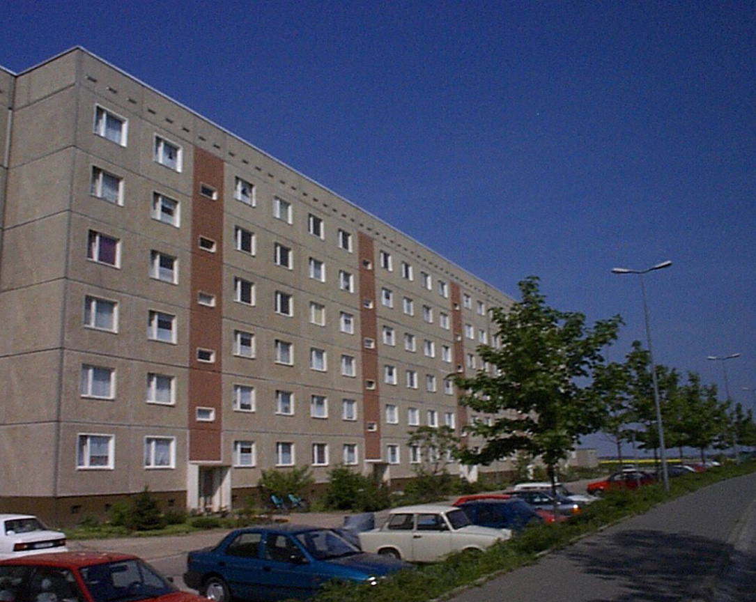 Ansicht eines sechsstöckigen unsanierten Mehrfamilienhauses im grünen Grundstück mit Parkflächen