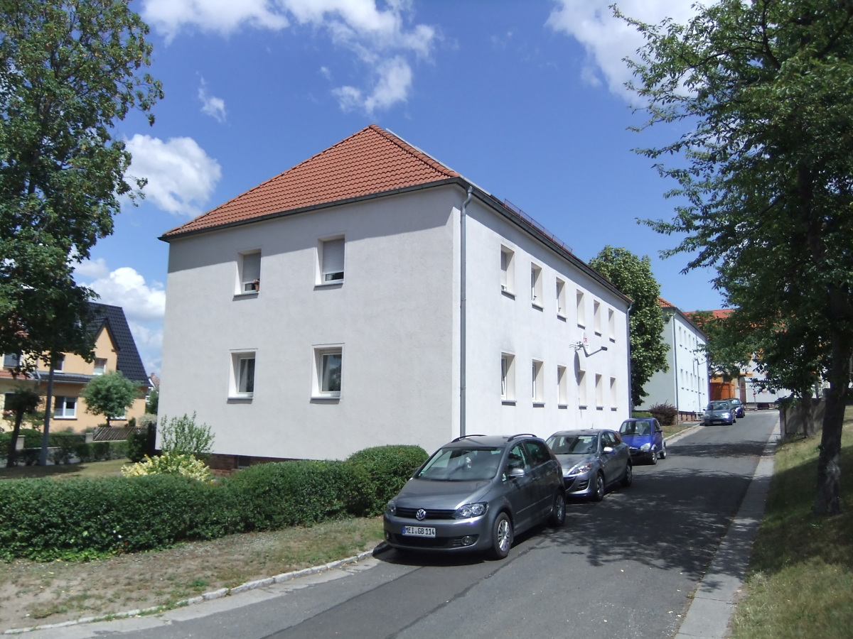 Straßenansicht eines zweistöckigen sanierten Mehrfamilienhauses im grünen Grundstück